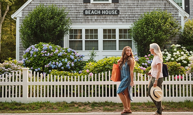Two women walking down the street in front of a beach house