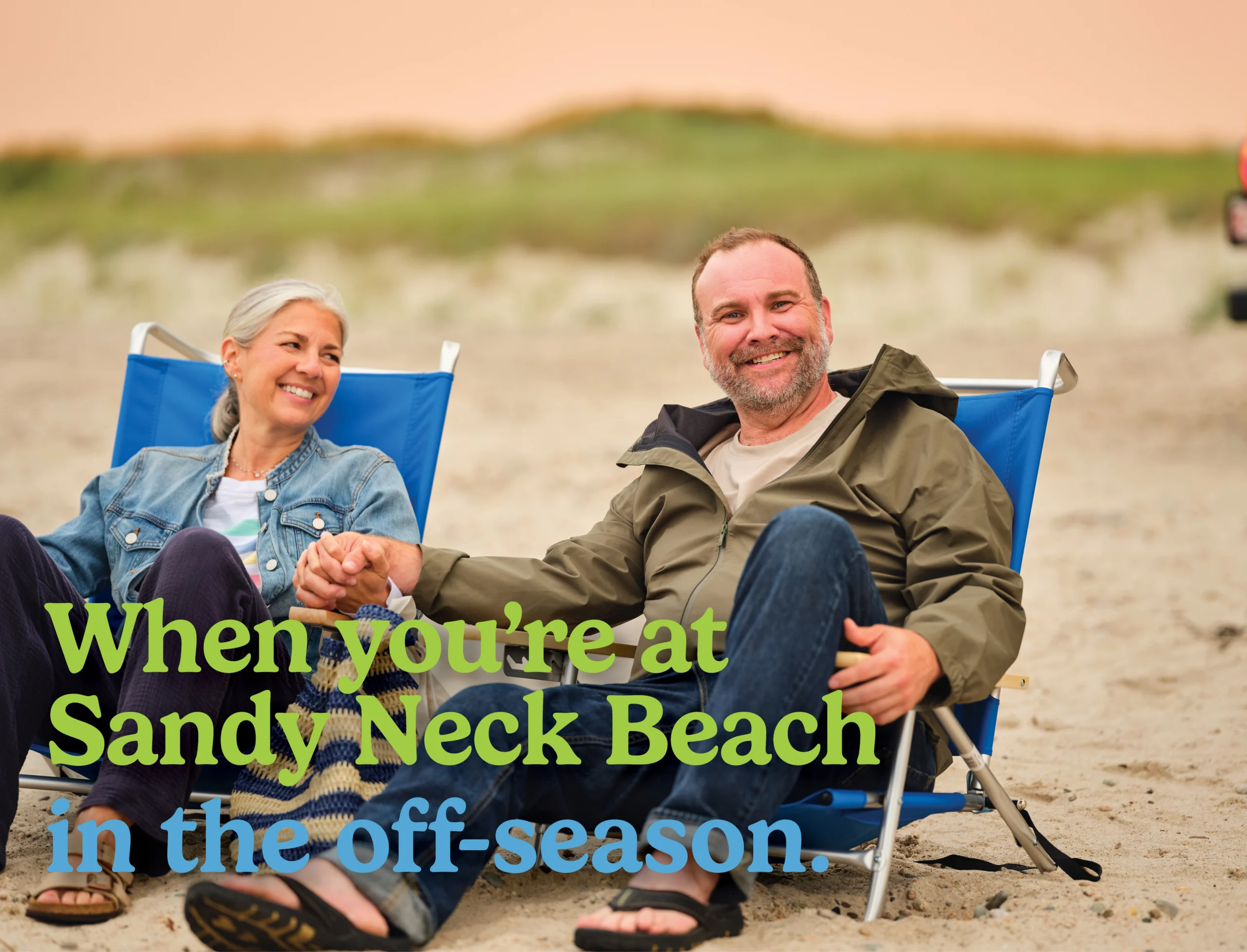Older husband and wife sit on beach chairs holding hands at Sandy Neck Beach. Text overlay reads: 'When you're at Sandy Neck Beach in the off-season'
