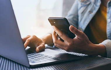 A close up of someone using their mobile phone and laptop