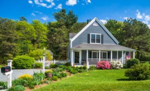 An American flag flies from the open porch and gardens surround a small single family home on a Spring afternoon on Cape Cod on the Massachusetts coast.