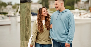 Young adult couple holding hands and smiling at each other walking boatyard