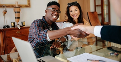 Man and woman sit at business desk shaking professional's hand