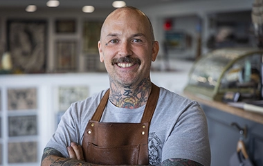 Local tatoo artist, Mark Corliss, stands with his arms crossed and smiling in his studio, Spilt Milk.