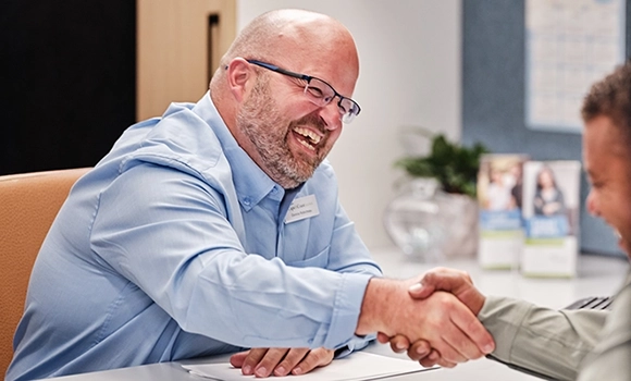 A Cape & Coast Bank employee shakes client's hand over desk