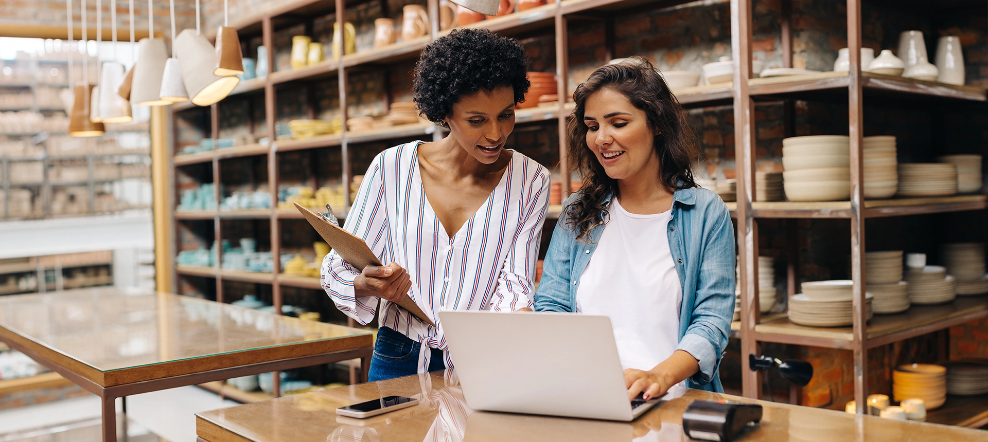 Two women with pottery behind them looking at a laptop