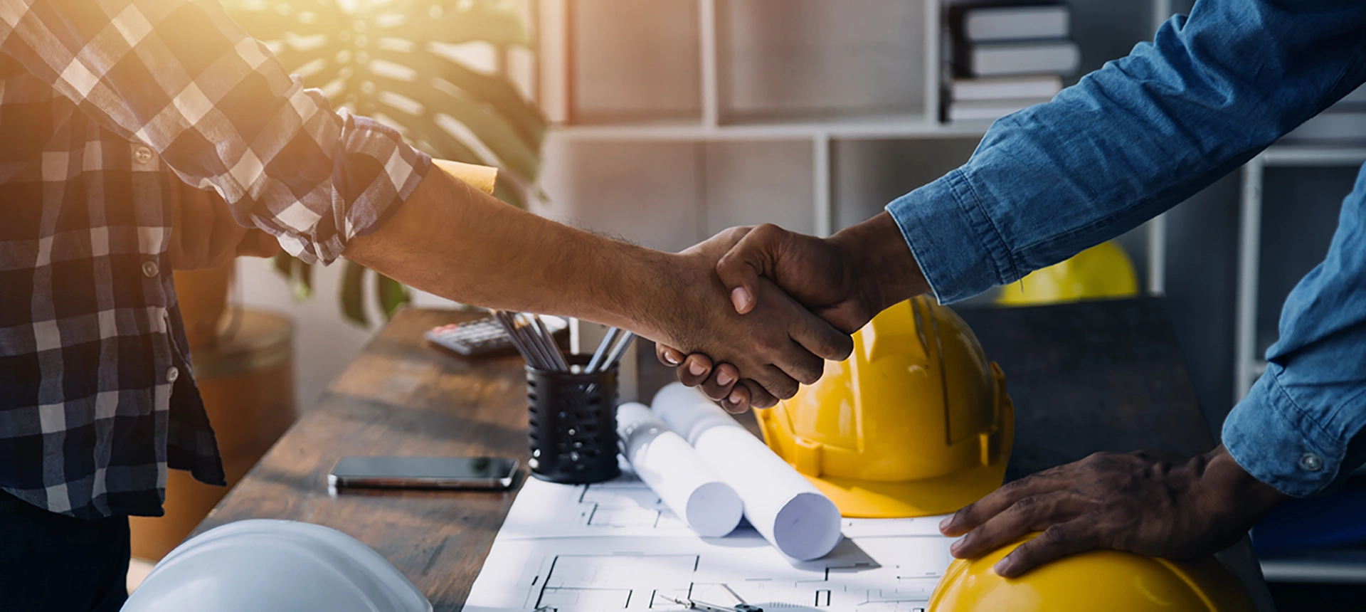 hands shaking over a table with blueprints