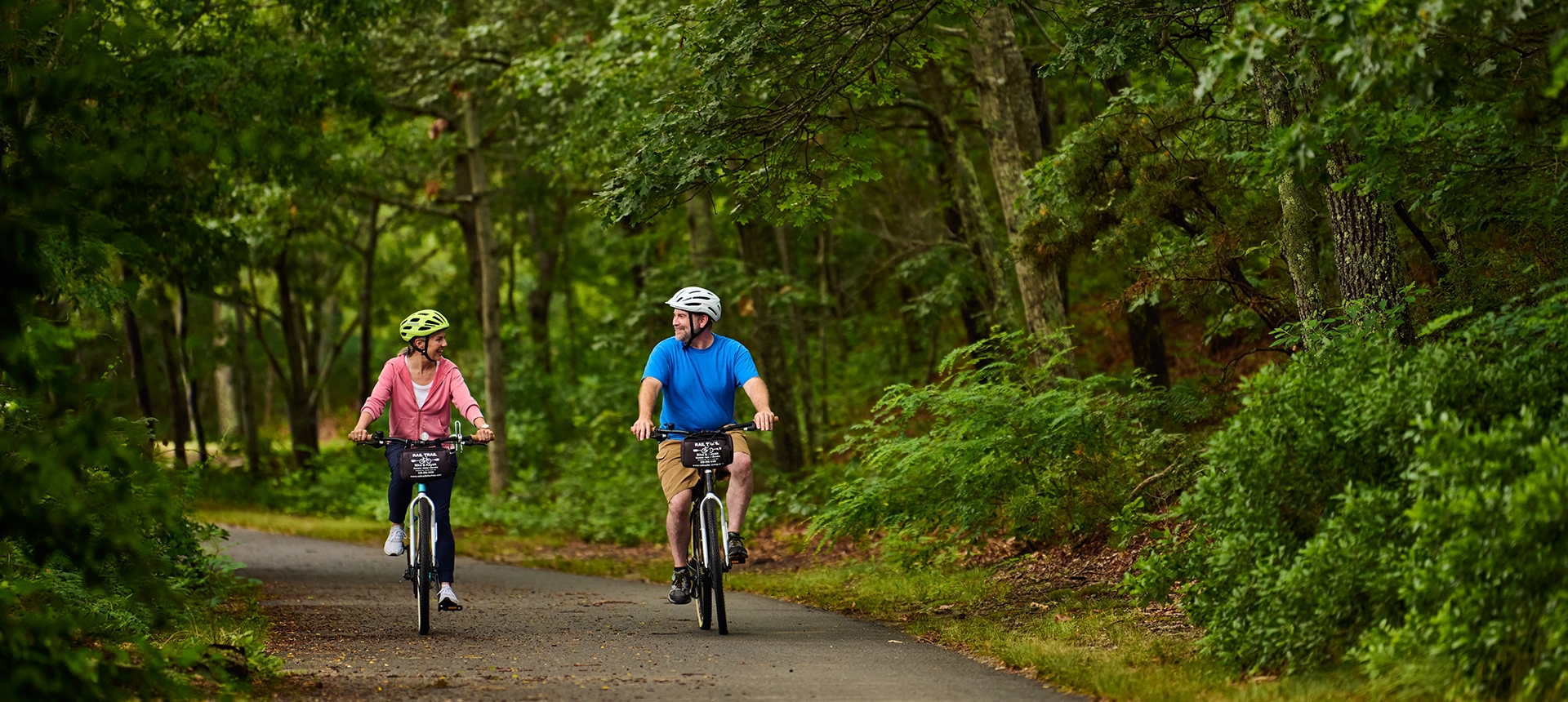 Adult male and female bike together on the Cape Cod Rail Trail.