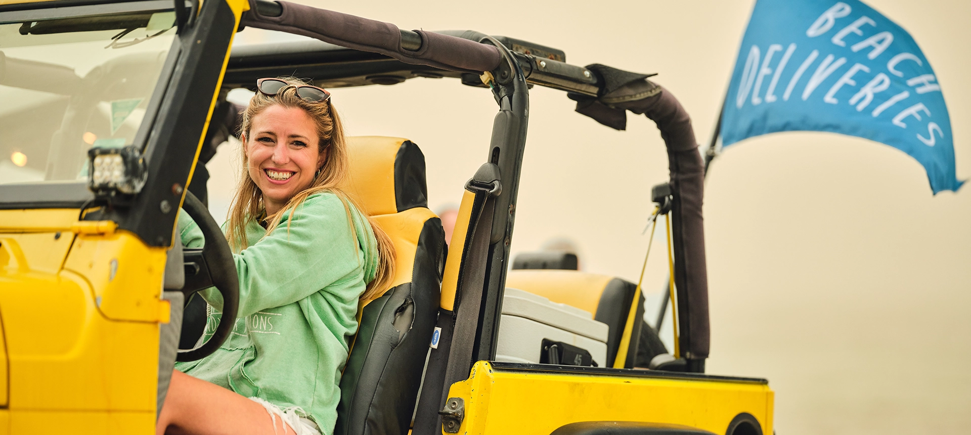 A woman in a yellow jeep on the beach
