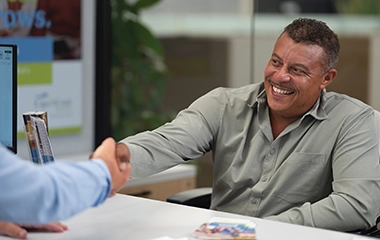 Man shaking bank representative's hand, sitting at bankers desk.