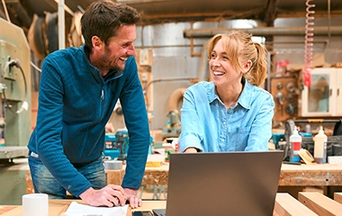 Two people in a workshop laughing behind a laptop
