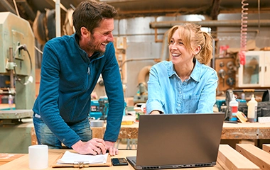 Two people in a workshop laughing behind a laptop