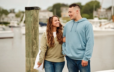 Young adult couple holding hands and smiling at each other walking boatyard