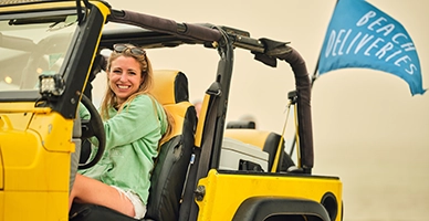 A woman in a yellow jeep on the beach